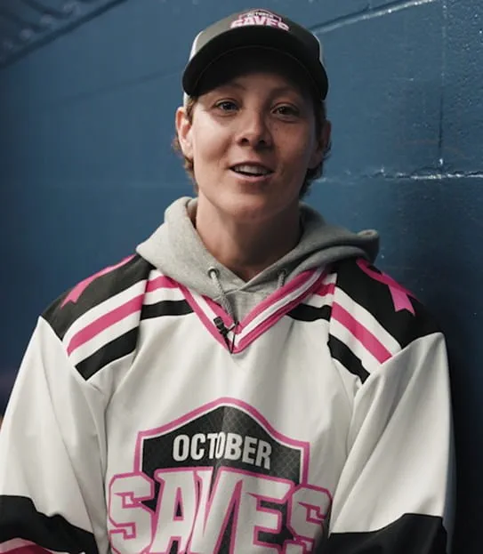 Erica Howe sitting on a bench in a locker room wearing an October Saves hockey jersey