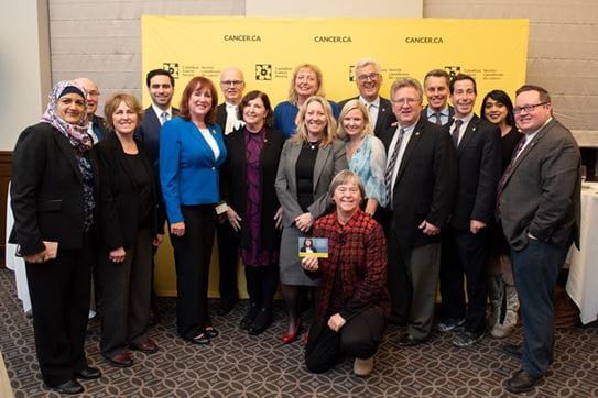 CCS staff and government officials pose together in front of a large yellow CCS banner   
