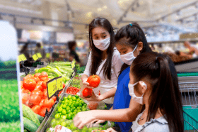 Une mère et ses deux enfants portent des masques protecteurs lorsqu’ils magasinent des fruits et légumes dans une épicerie