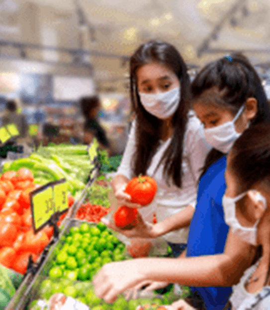 Une mère et ses deux enfants portent des masques protecteurs lorsqu’ils magasinent des fruits et légumes dans une épicerie