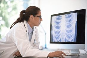 Une femme médecin assise à son bureau regardant le radiogramme d’un thorax sur son ordinateur.