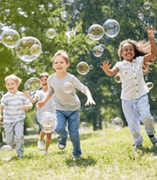Young children smiling and enjoying a warm, sunny day by chasing soap bubbles