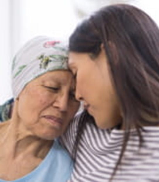 Une femme âgée atteinte d’un cancer et portant un couvre-chef, dans une étreinte avec sa fille adulte