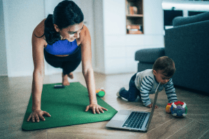 A mom exercises while her child plays on the floor next to her.