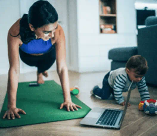 A mom exercises while her child plays on the floor next to her.