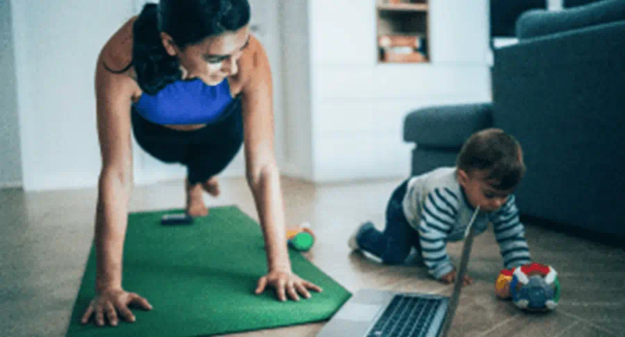 A mom exercises while her child plays on the floor next to her.