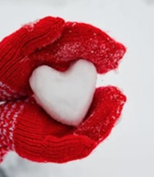 Mains dans des mitaines rouges tenant un cœur fait de neige.