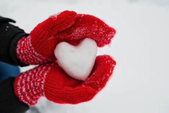 Hands in red mittens holding heart made out of snow