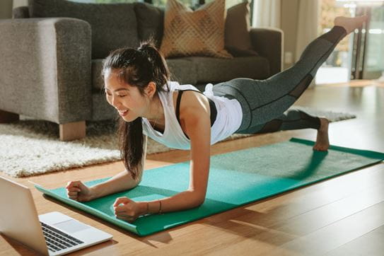 a woman does yoga while watching her laptop screen