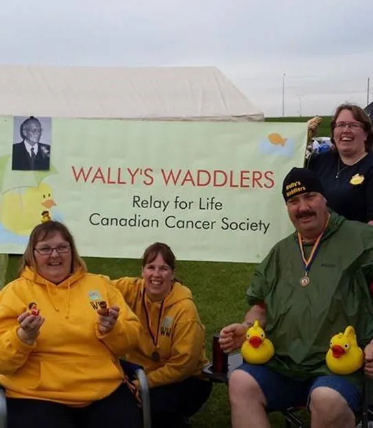 Cinq personnes tenant des canards de plastique, assis autour d’une affiche où on peut lire « Wally’s Waddlers » Relais pour la vie, Société canadienne du cancer.