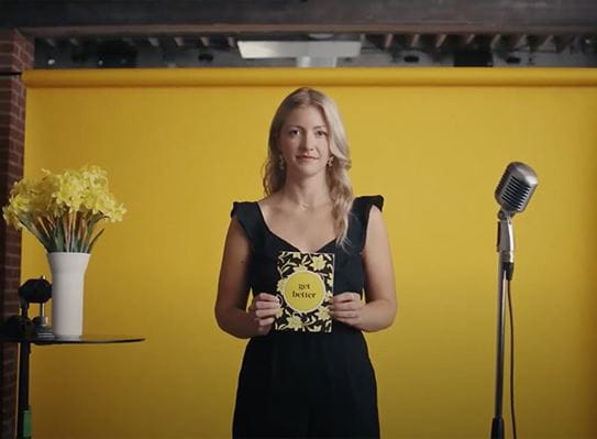 A woman holds up a get better card while standing beside a vase of daffodil. 