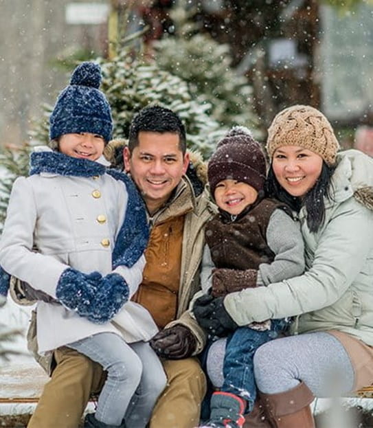 A family sitting together outside in the snow wearing winter jackets and hats
