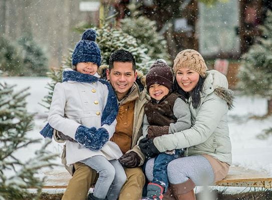 A family sitting together outside in the snow wearing winter jackets and hats