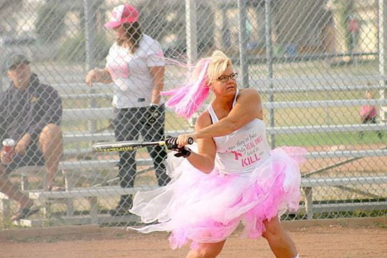Une femme en grande jupe rose avec des cheveux teints roses balançant un bâton de baseball