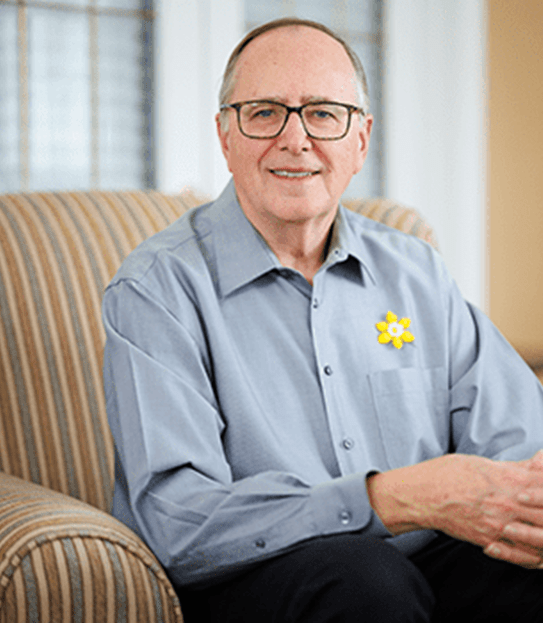 Photo of Allen Goudie wearing a daffodil pin on his shirt, sitting in an armchair.