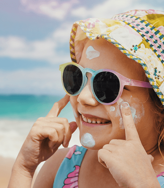 Une jeune fille mettant de la crème solaire sur une plage.