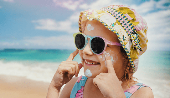 A young girl putting on sunscreen on a beach. 