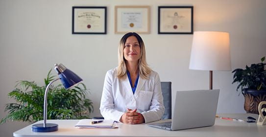La chercheuse April Khademi, Ph. D., est assise à un bureau, les mains jointes.