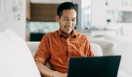 A person wearing an orange shirt looks down at a computer screen.