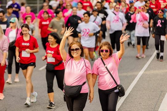 Two women wave while walking in the Run for the Cure