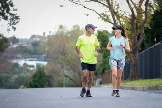 A woman and man smile while running outside