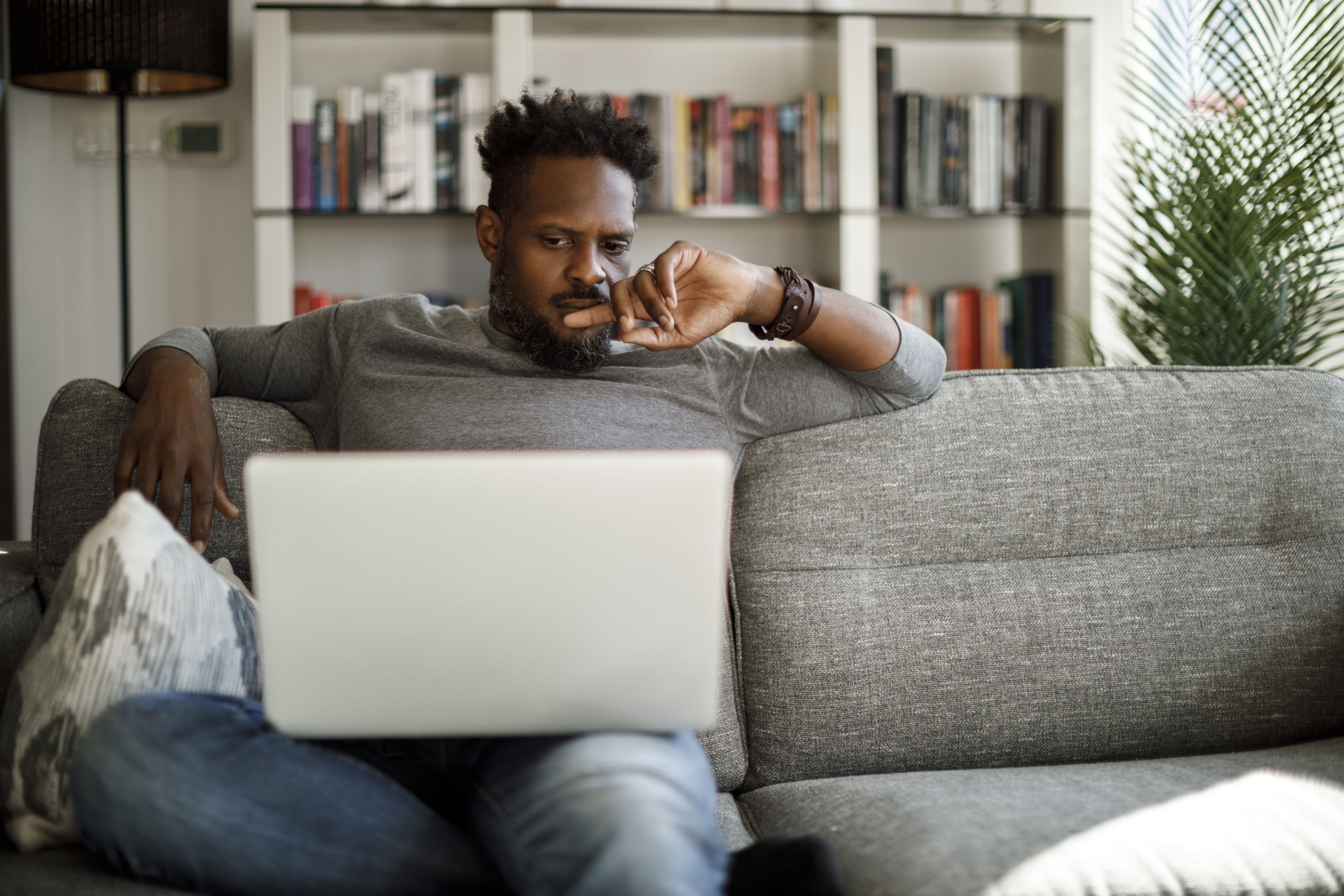 Man sitting on couch looks confused at his computer