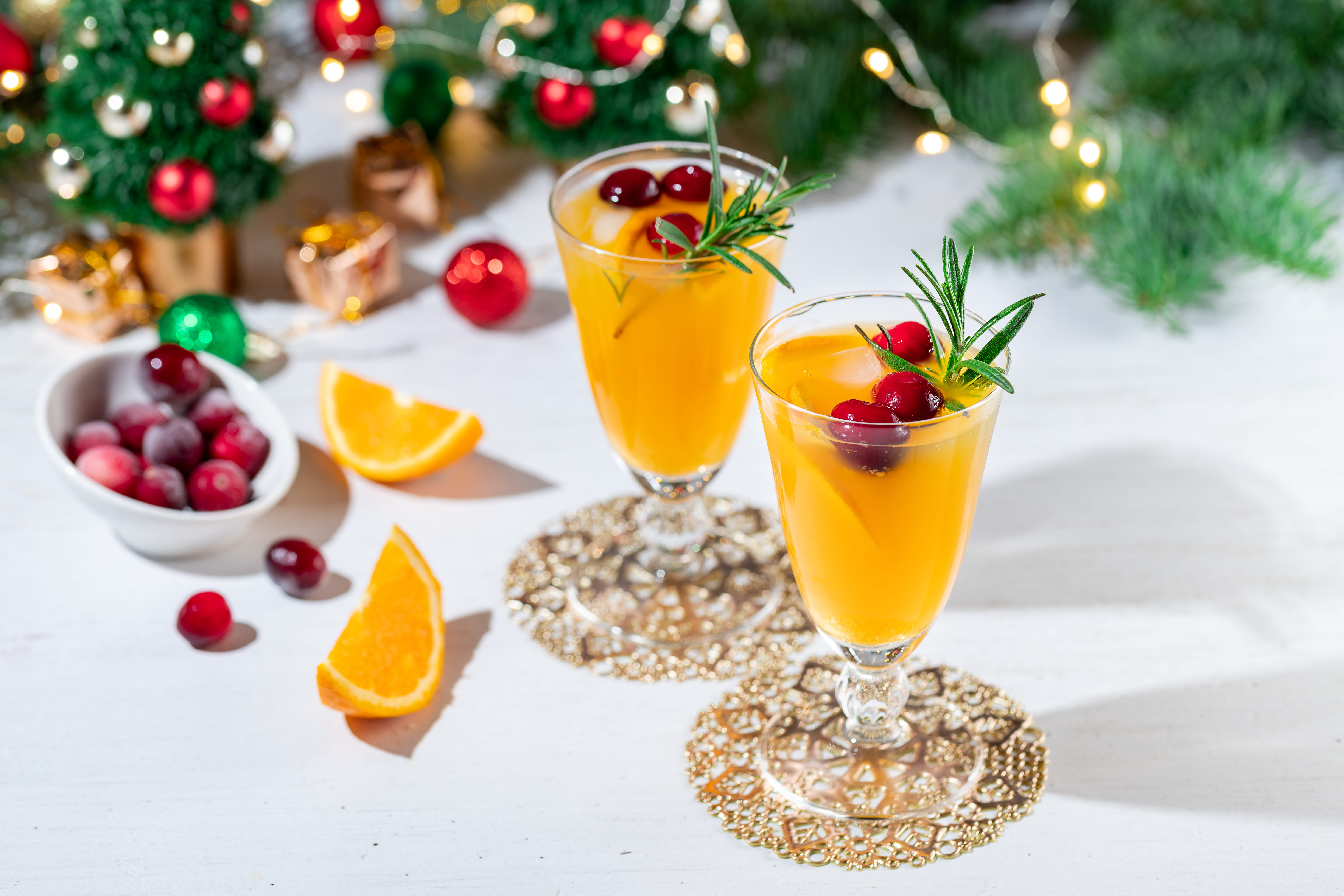 Two orange drinks with cranberries and a sprig of ming