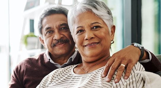 A person has their arm around their partner and they are both seated on a couch.
