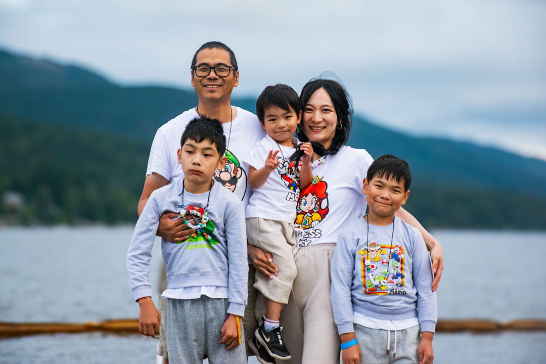 Kate, Daniel and their 3 sons posing in front of a lake and mountain.