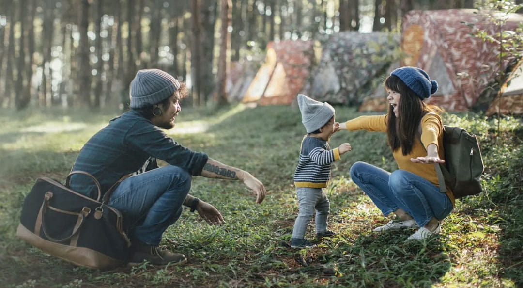 Deux parents jouant avec leur enfant dans une forêt.