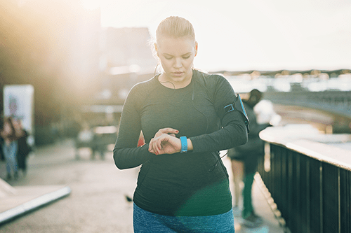 Une femme en tenue de sport faisant de la course pied à l’extérieur regarde sa montre intelligente.