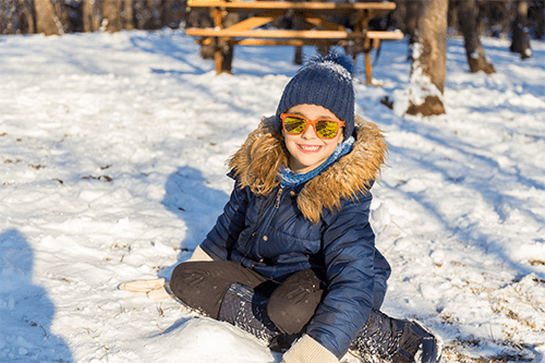 A kid wearing sunglasses and sitting in the snow