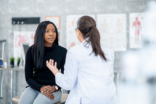 A young woman sitting on an examination table, talking to her doctor