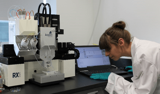 A female scientist stands next to a 3D printer 