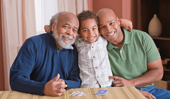 A young boy smiling and sitting between his father and his grandfather