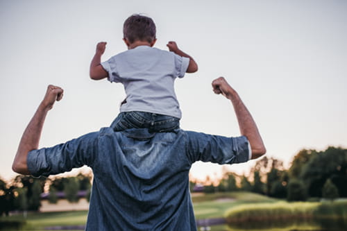 A young boy sits on top of his father’s shoulders 