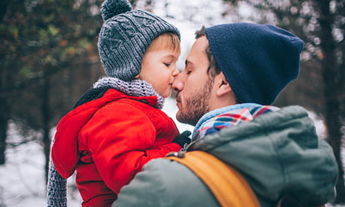 A father is holding his young son and their noses are touching.