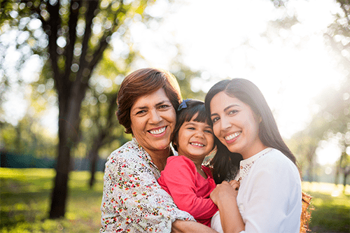 A grandmother, daughter, and granddaughter hugging in a park.