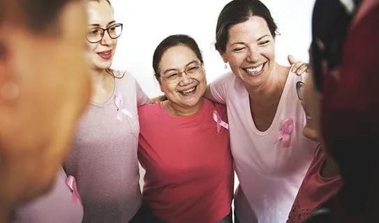 A group of women wearing pink with the arms around each other’s shoulder