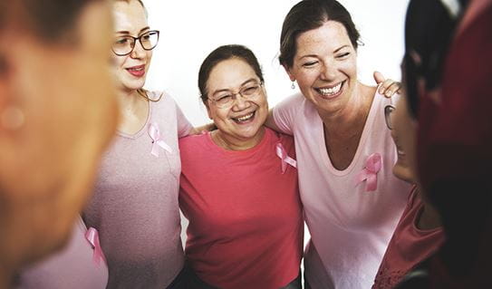 A group of women wearing pink with the arms around each other’s shoulder 