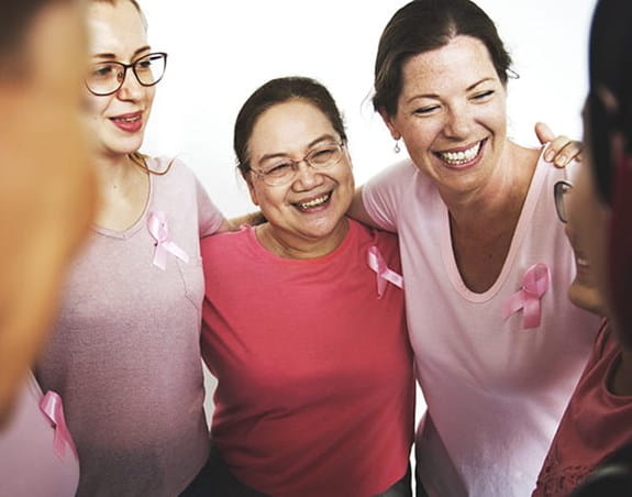 A group of women wearing pink with the arms around each other’s shoulder 