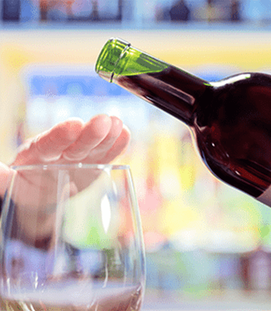 Hand above a glass, blocking a wine bottle.