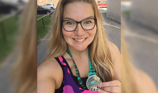 Une jeune femme blonde sourit en montrant une médaille d’argent gagné lors d’une course