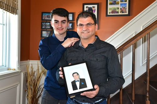 Denis Dupuis holding a photo and standing with his teenage son