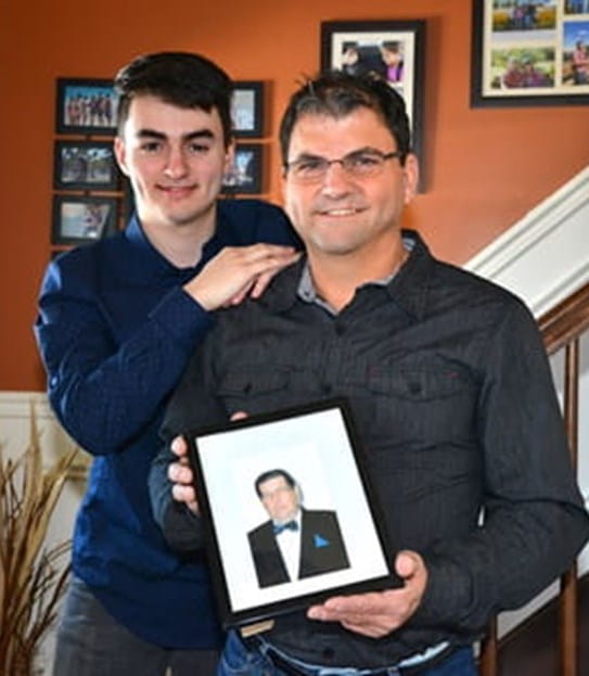 Denis Dupuis holding a photo and standing with his teenage son