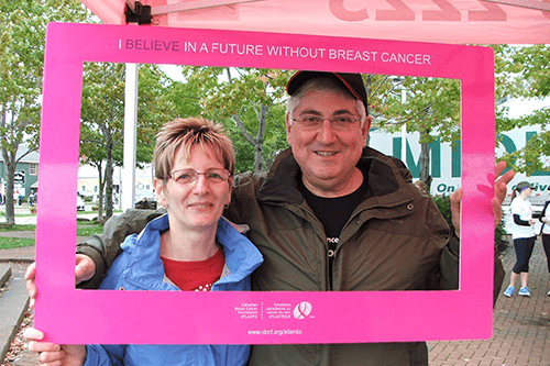 A man and woman posing while holding a pink breast cancer awareness frame.