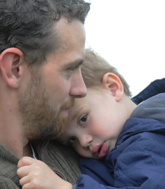 Tyler tenant son fils, dont la tête repose sur son épaule.