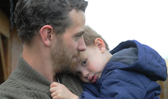 Tyler tenant son fils, dont la tête repose sur son épaule.