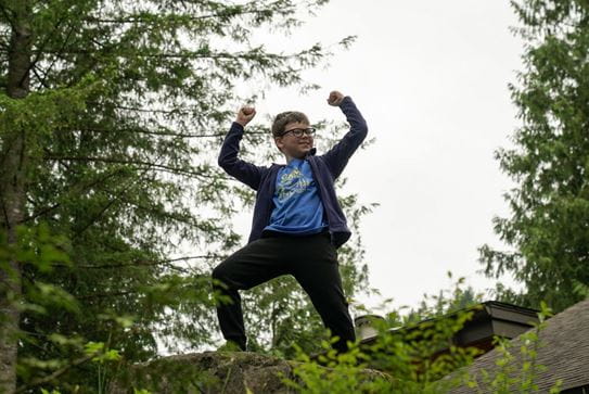 Un petit garçon debout sur un rocher, les mains en l’air, triomphant.