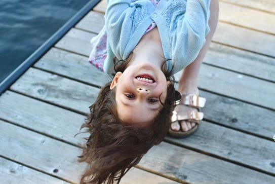 A little girl laughing while being held upside down by an adult.